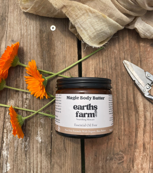 Jar of Magic Body Butter from Earth's Farm on a wooden surface with orange flowers and a cloth.