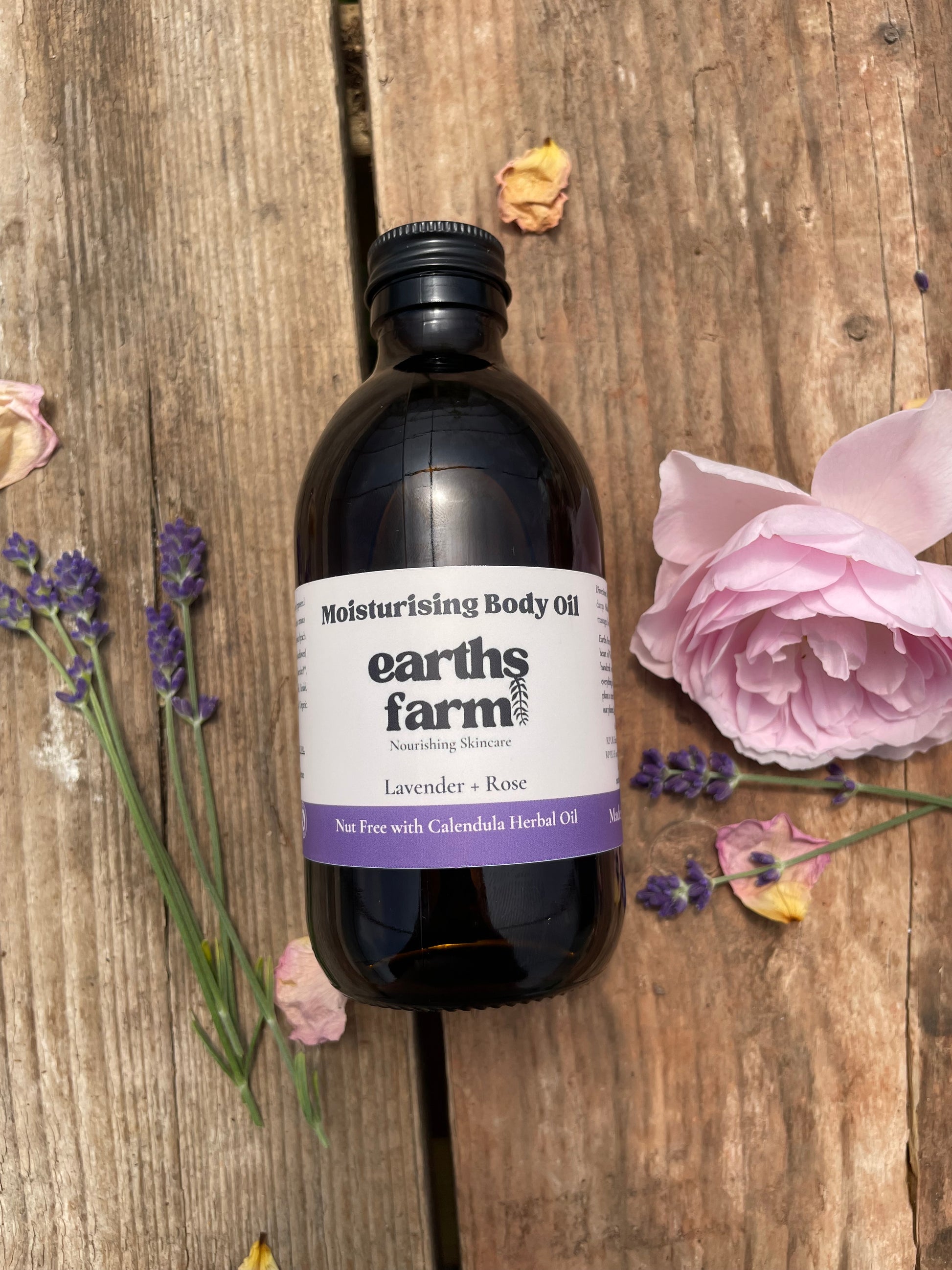 Bottle of Earth's Farms body oil on a wooden surface with flowers