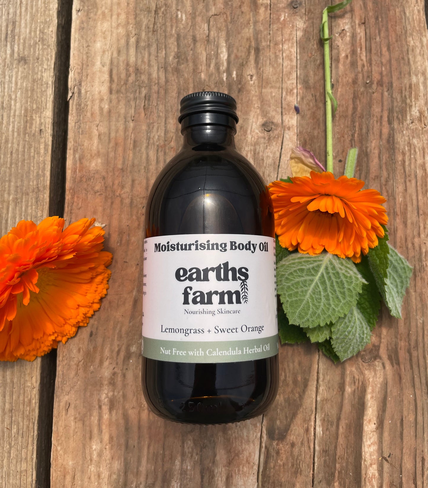 Bottle of Earth's Farm body oil on a wooden surface with flowers.