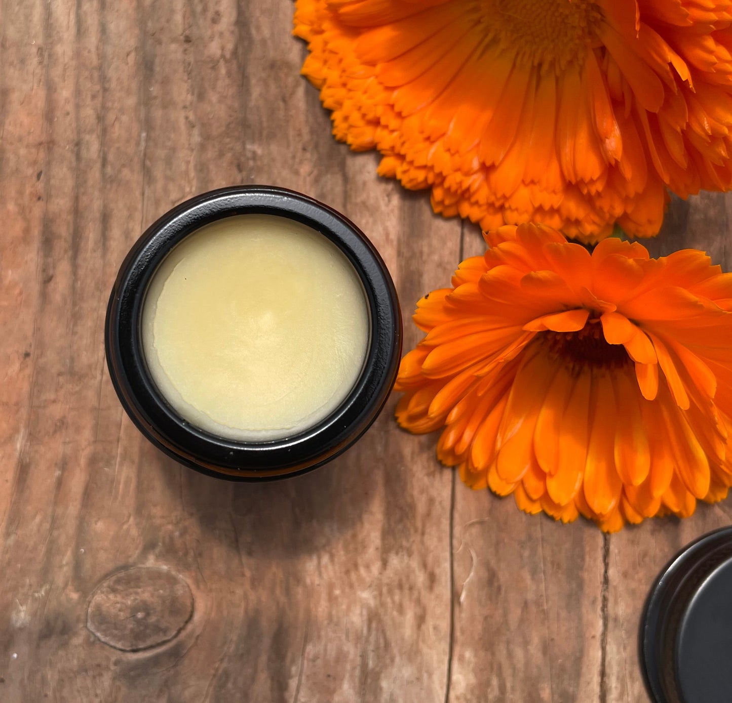 amber glass container with balm surrounded by orange flowers on wooden surface