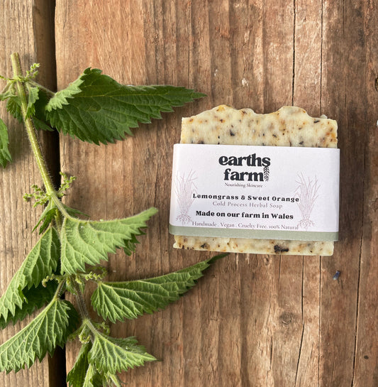 Bar of soap with a label on a wooden surface, surrounded by green leaves.