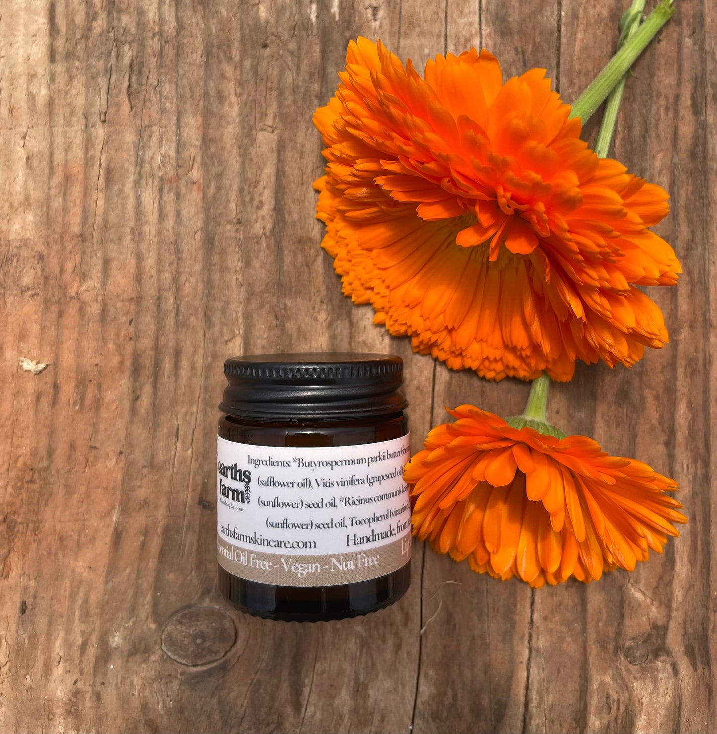Small jar with a label next to two orange flowers on a wooden surface
