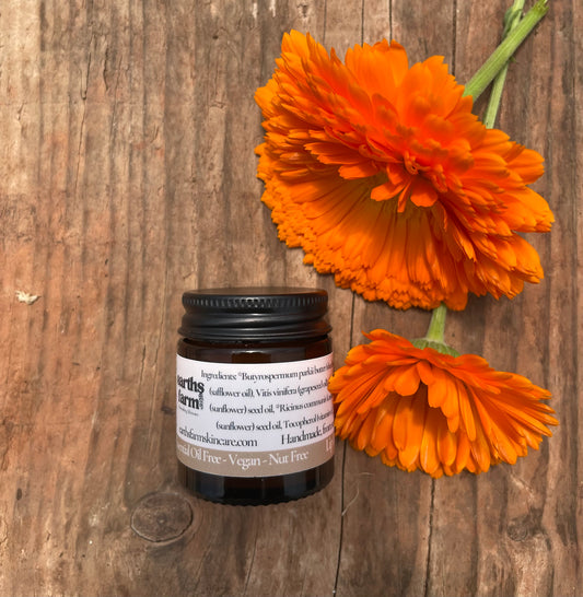 Small jar with a label next to two orange flowers on a wooden surface